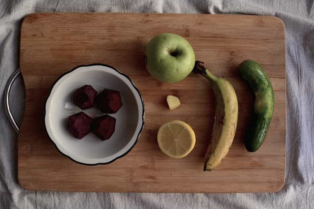 Beets, lemon, green apple, ginger, banana and cucumber in a wooden cutting board.