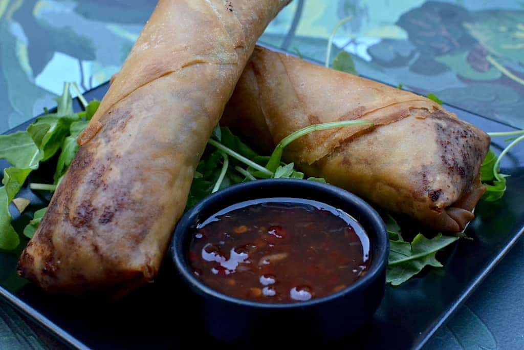 2 Spring rolls with sauce and greens in a black plate