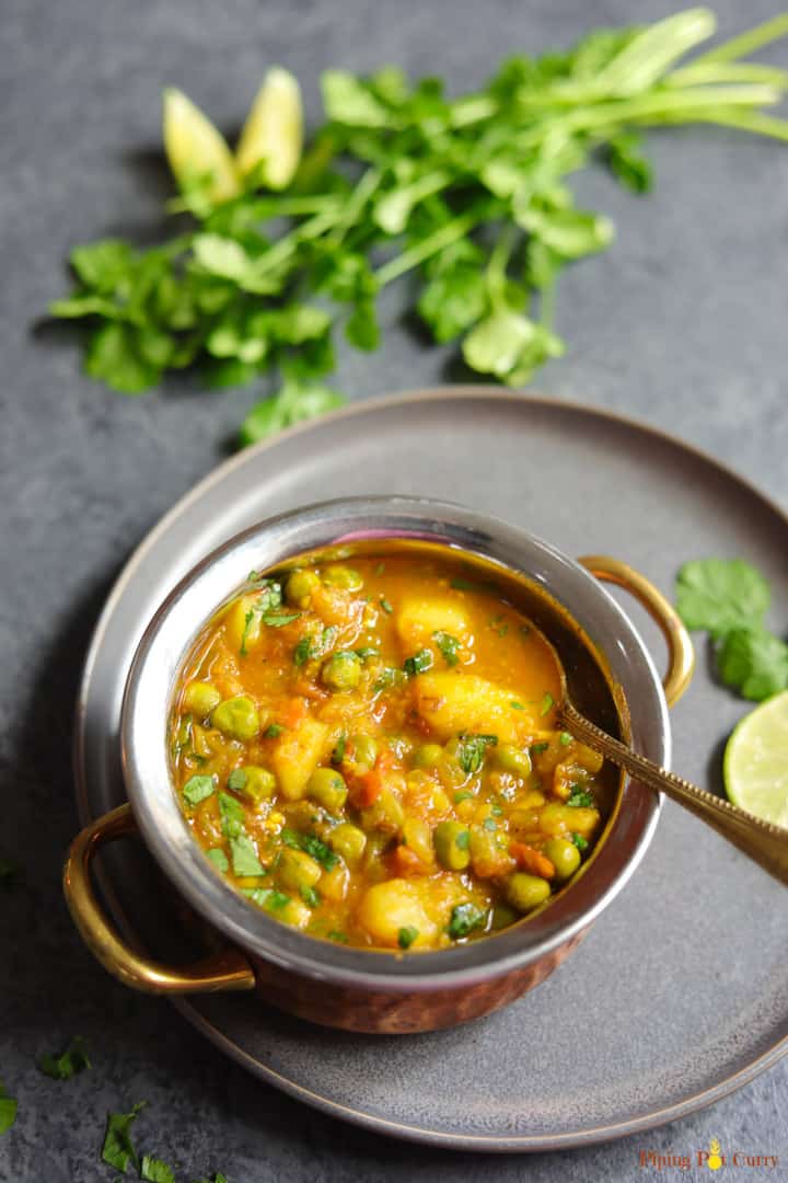 potato and peas curry in a grey plate and greens on the side