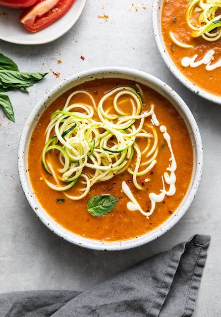 tomato soup with curry and green noodles in a white bowl