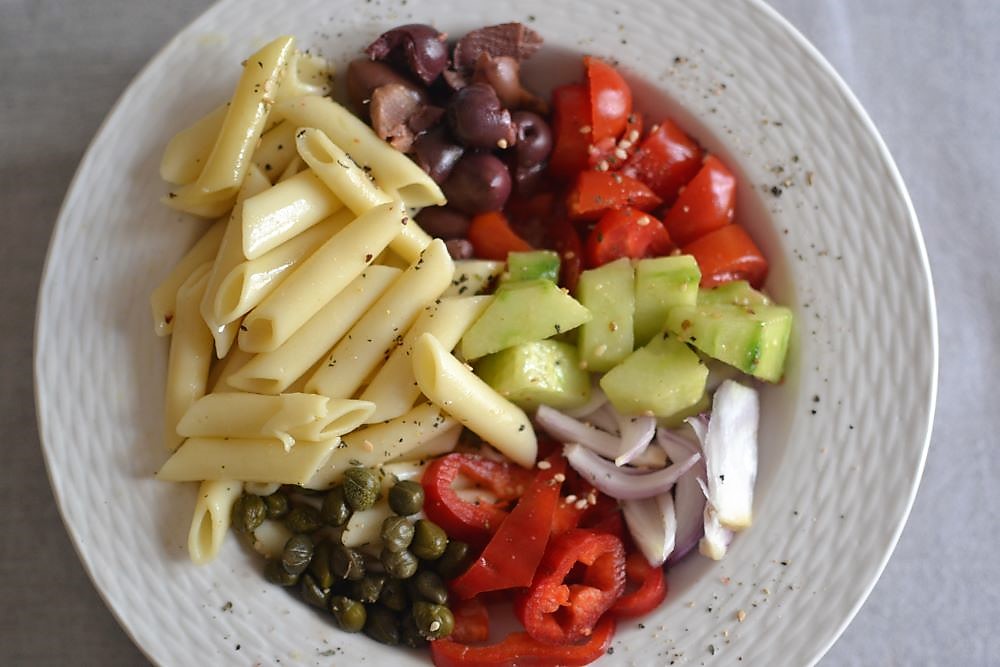 pasta, olives, tomatoes, cucumber, peppers in a white plate