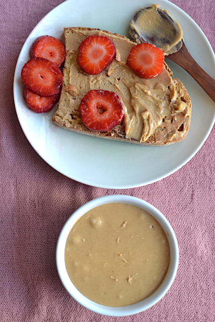cashew butter in a white bowl and a slice of bread with butter and strawberries